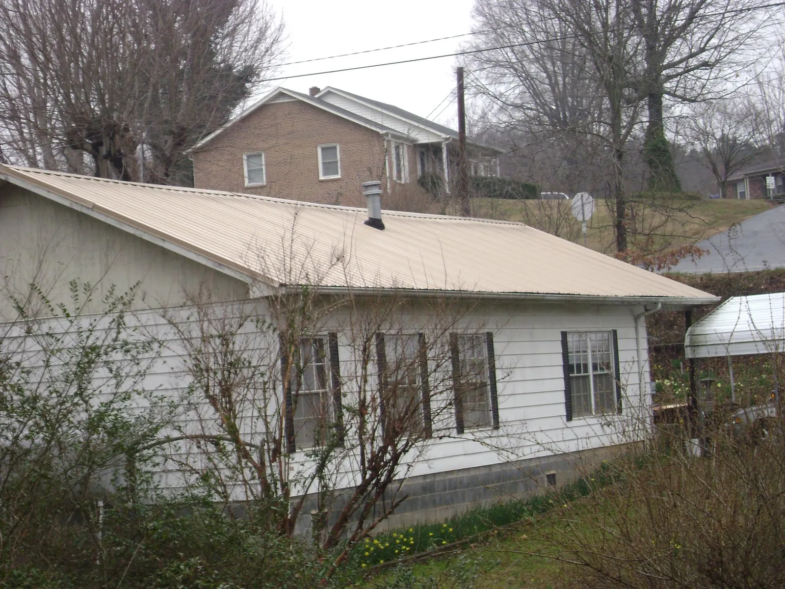 Tan metal roof on a white sided house set into a hillside — Commercial Roofing by Roofing Brothers in Sylvania